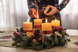 Mujer encendiendo la cuarta vela de una corona de Adviento durante la Nochebuena.